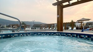 A pool area with a wooden pergola, lounge chairs, and a view of the mountains in the background.
