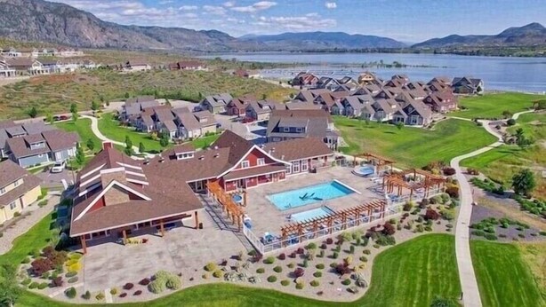 A residential area with houses, a swimming pool, and a lake in the background.