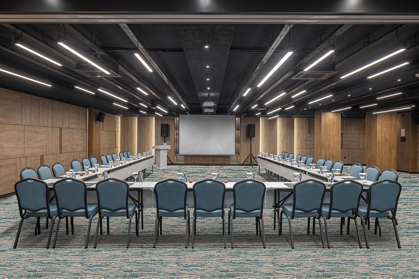 Un salón de conferencias con una larga mesa, sillas, una pantalla de proyector y un atril.