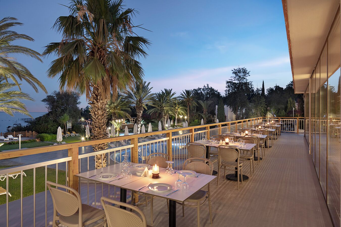 A restaurant with outdoor seating overlooking a pool and palm trees.
