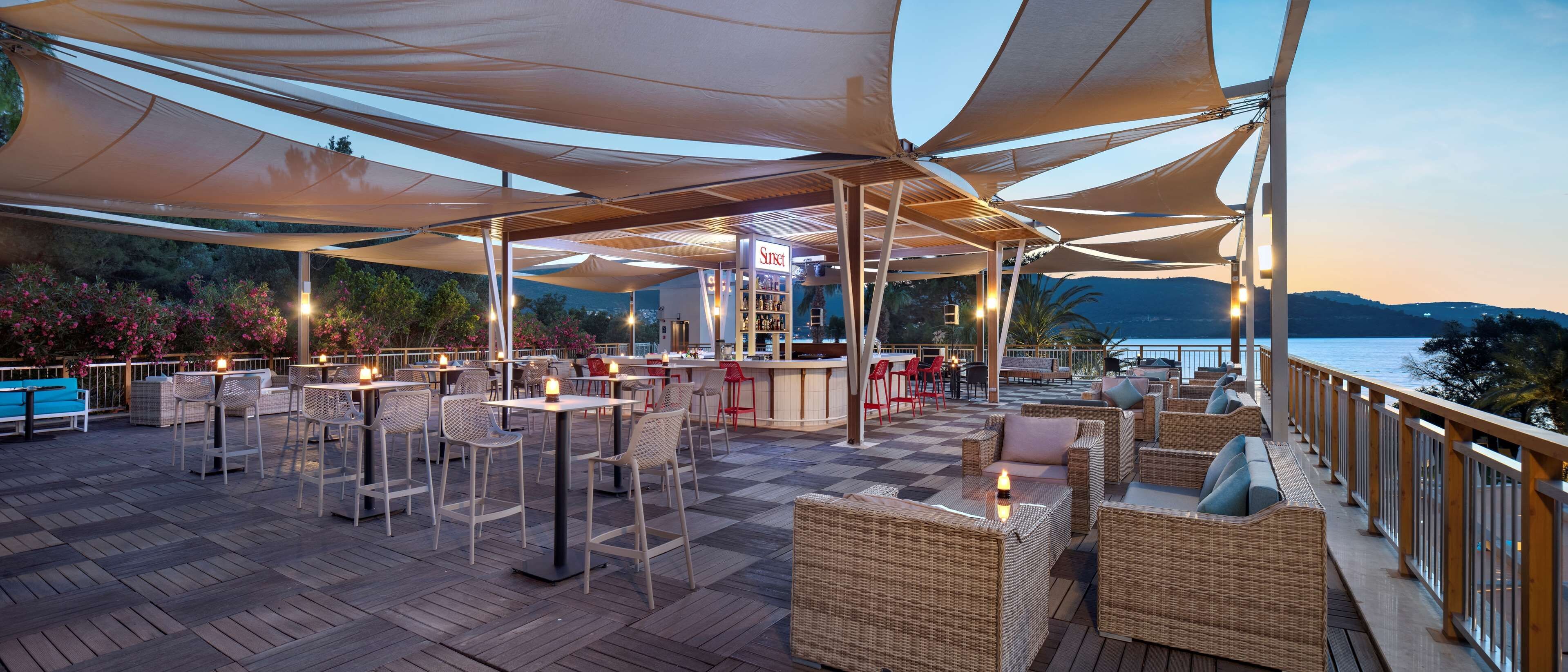 Un espacio al aire libre con mesas, sillas, un bar y vistas al agua.