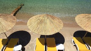 Uma praia com águas cristalinas, guarda-sóis de palha e cadeiras de praia amarelas.