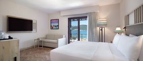 Habitación de hotel con cama, televisión, un cuadro, balcón con vistas y una lámpara.