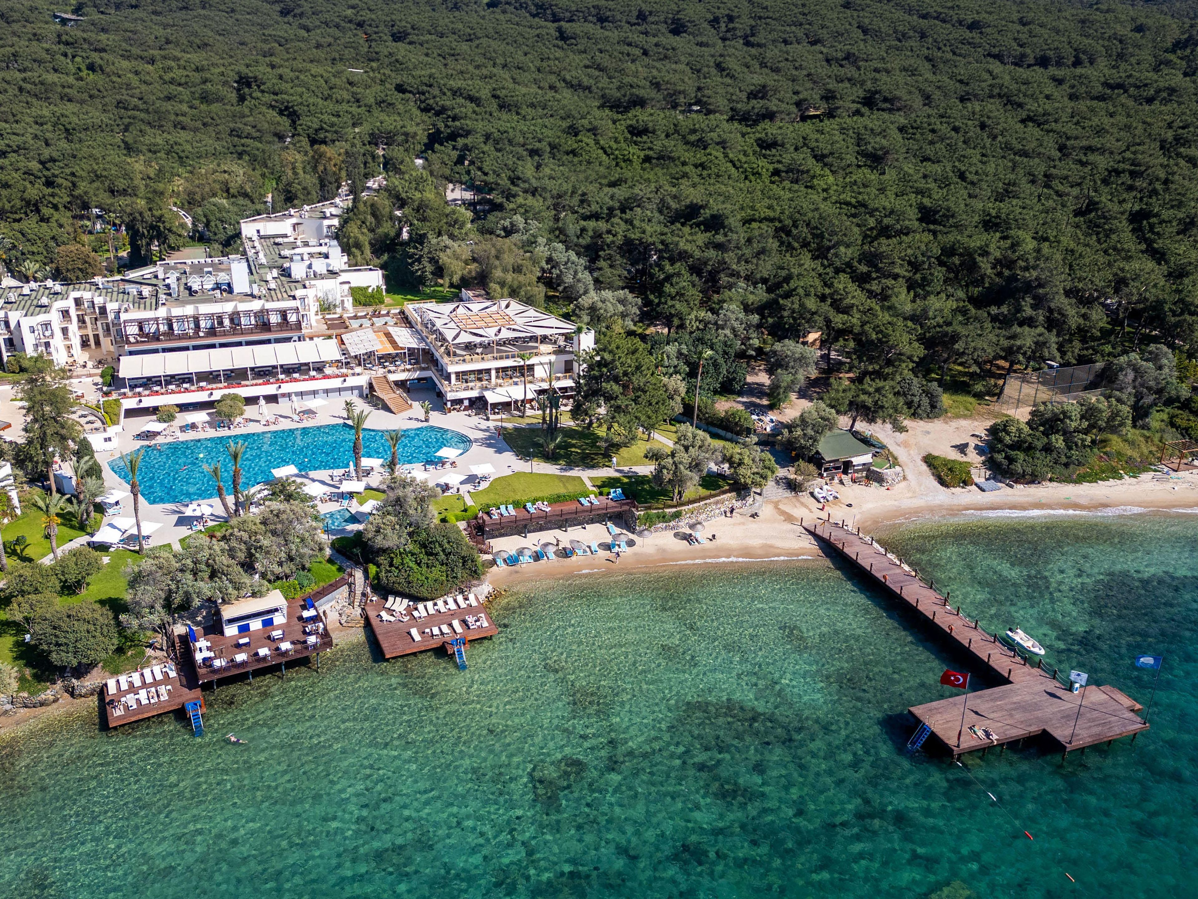 An aerial view of a resort with a large swimming pool, beach, and pier.