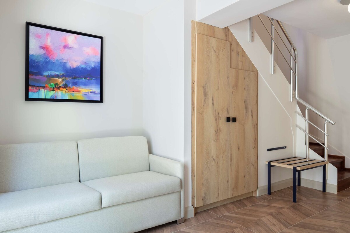 Una sala de estar moderna con un sofá, una puerta de madera, una escalera y un ventanal con vistas.