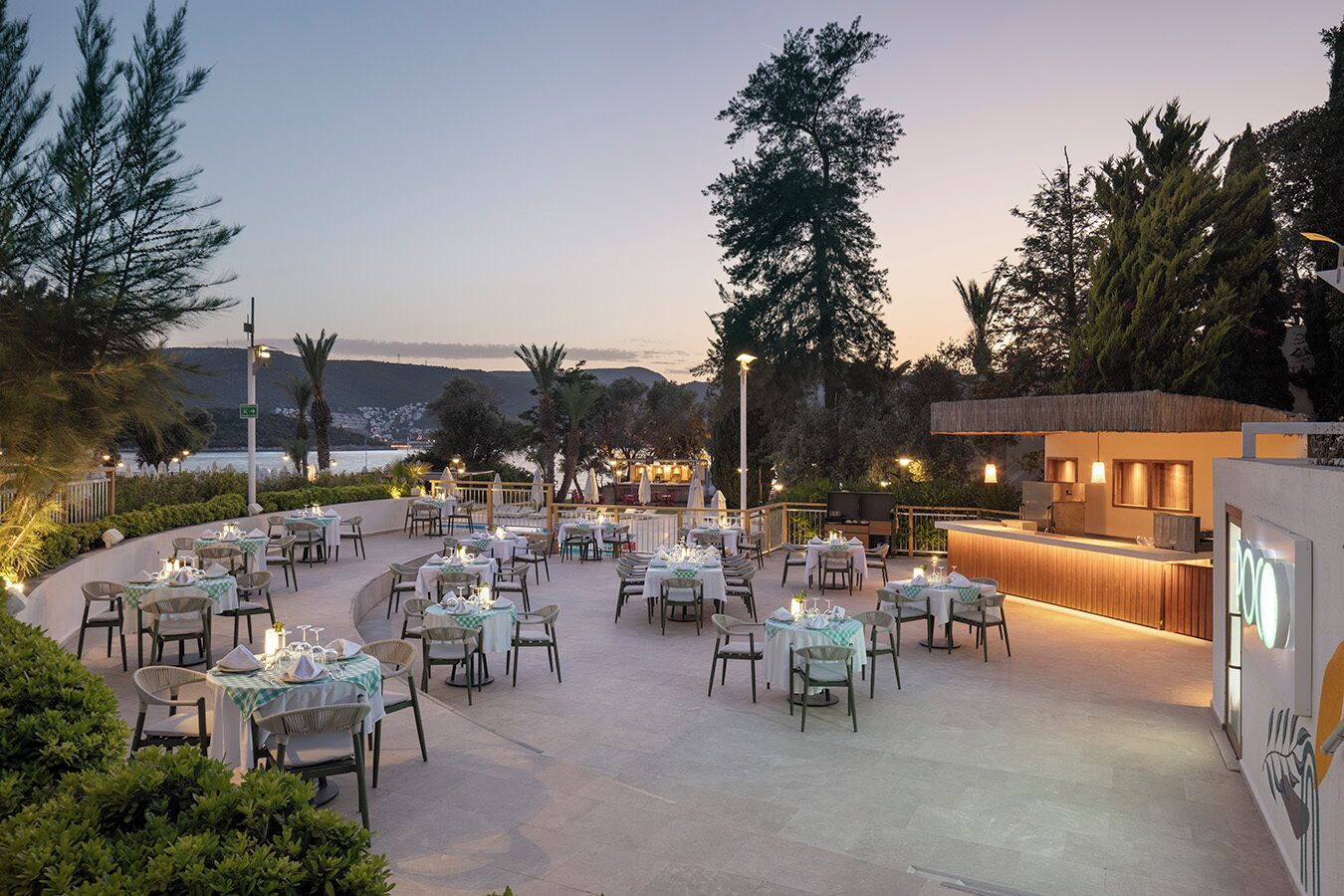 An outdoor dining area with tables and chairs, a bar, and a view of the sea.