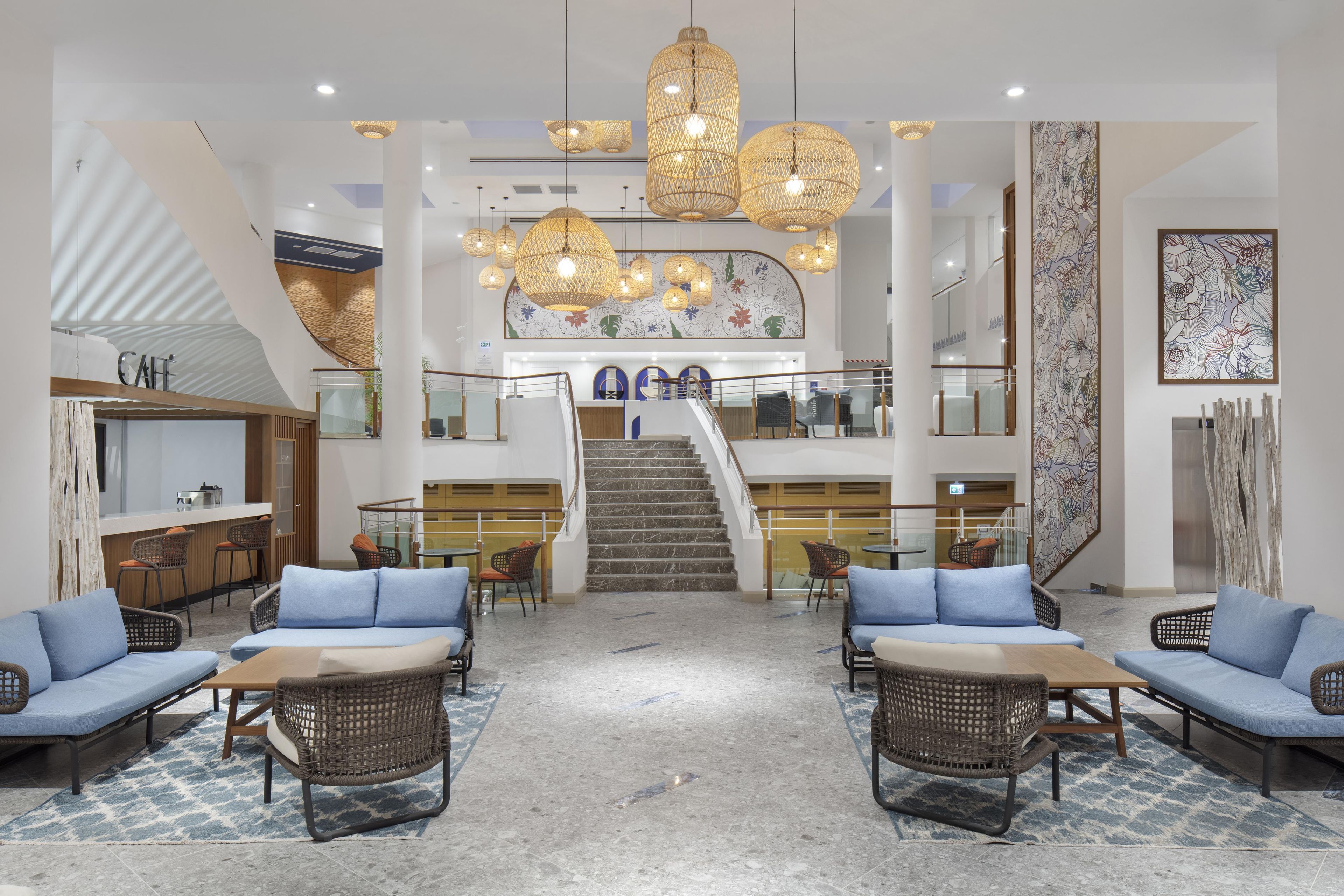 Un vestíbulo de hotel con una escalera central, zonas de estar y un mostrador de recepción.