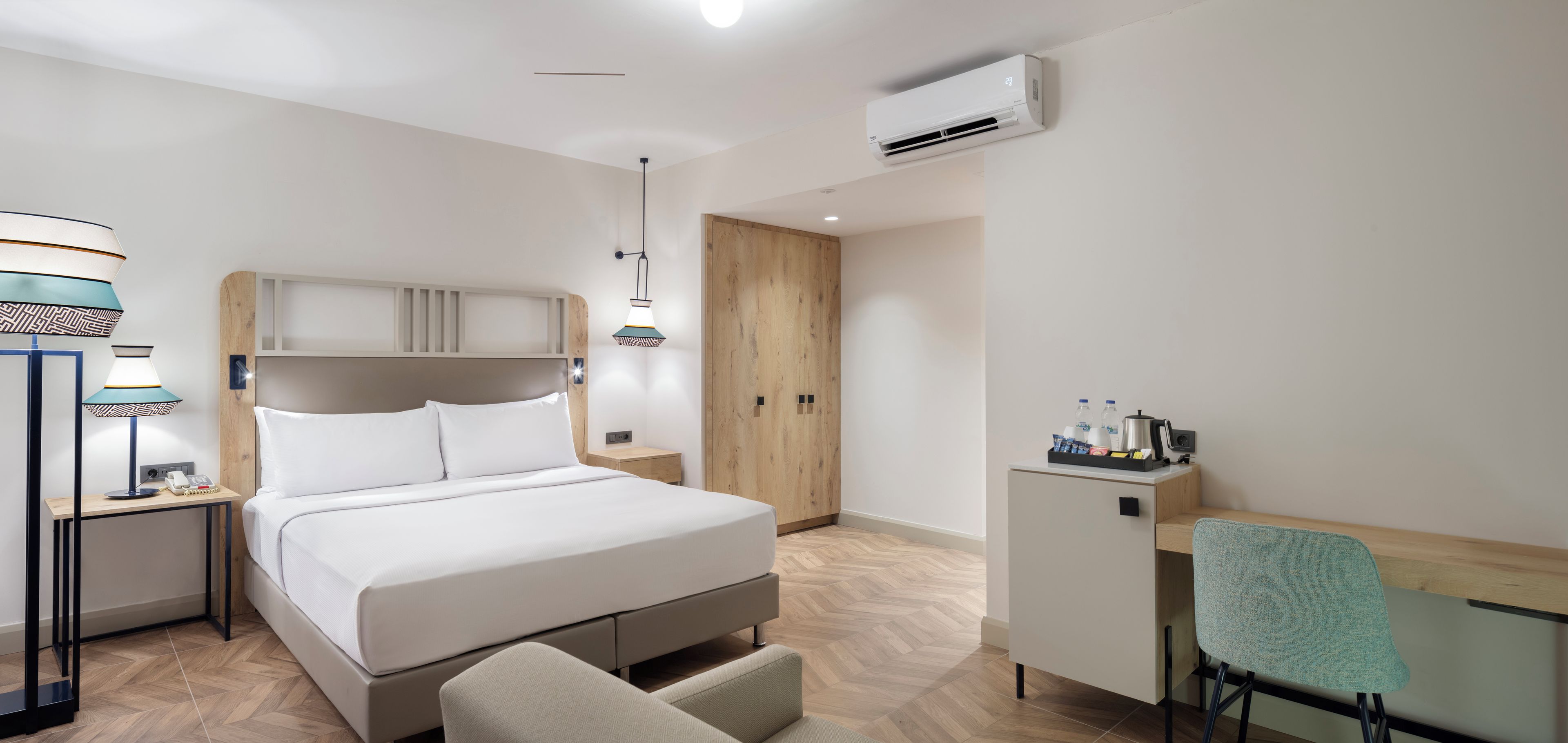 Una habitación de hotel moderna con cama, mesita de noche, lámpara, escritorio, silla, armario y equipo de aire acondicionado.