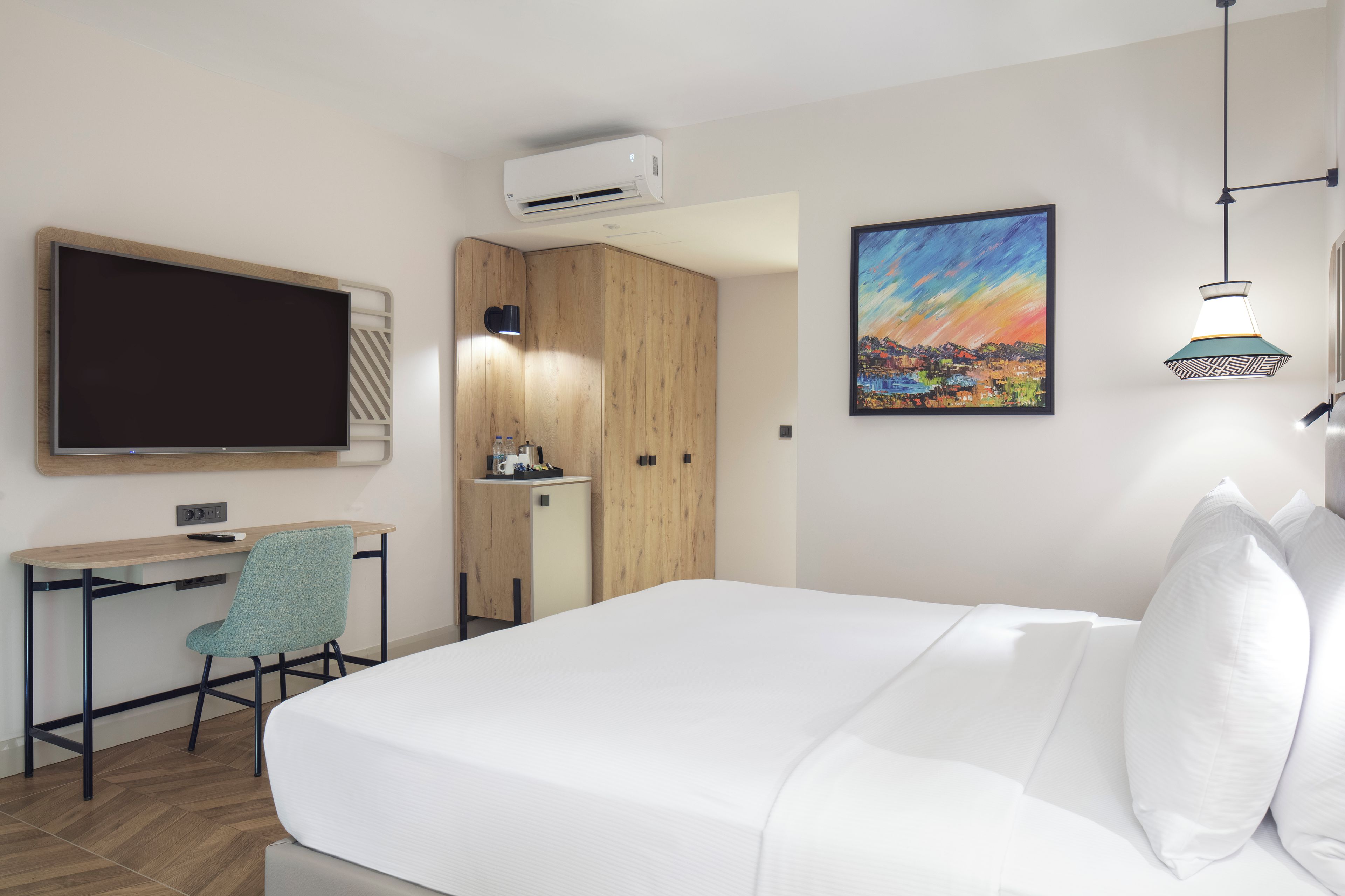 Habitación de hotel con cama, escritorio, silla, televisión, un cuadro y aire acondicionado.