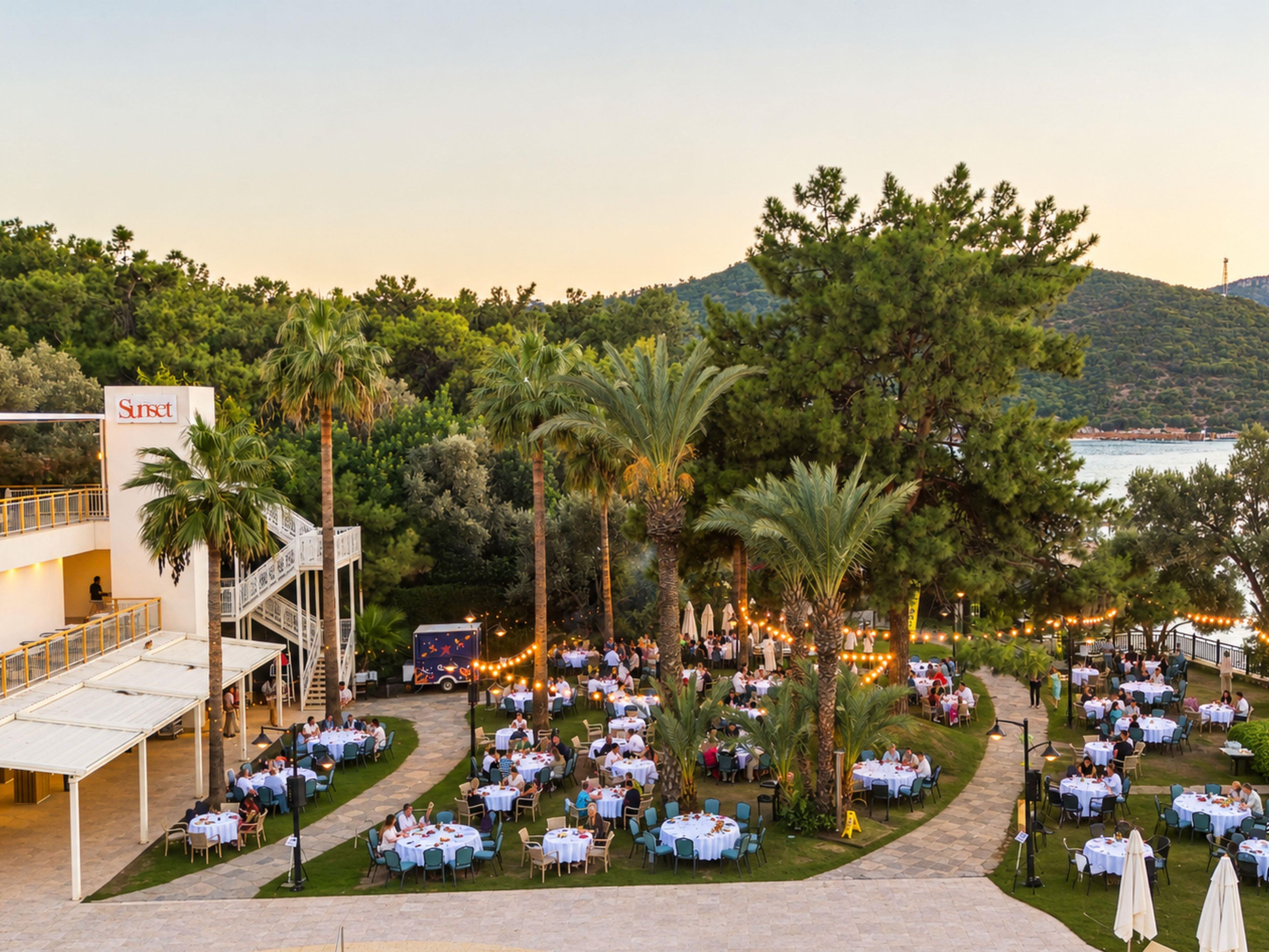 An outdoor dining area with multiple tables and chairs, surrounded by palm trees and a view of the sea.