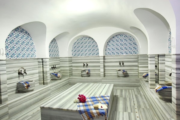 A bathroom with three sinks, each with a mirror and a towel. The walls have a marble pattern, and there are three arched windows with a blue and white pattern. - DoubleTree by Hilton Bodrum Işıl Club Ultra All Inclusive Resort (Bodrum)