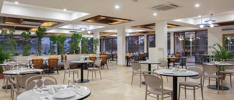 A spacious restaurant with round tables, chairs, and potted plants.