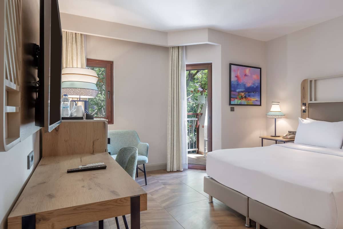 A hotel room with a large bed, a desk, a chair, a TV, a lamp, and a painting on the wall.