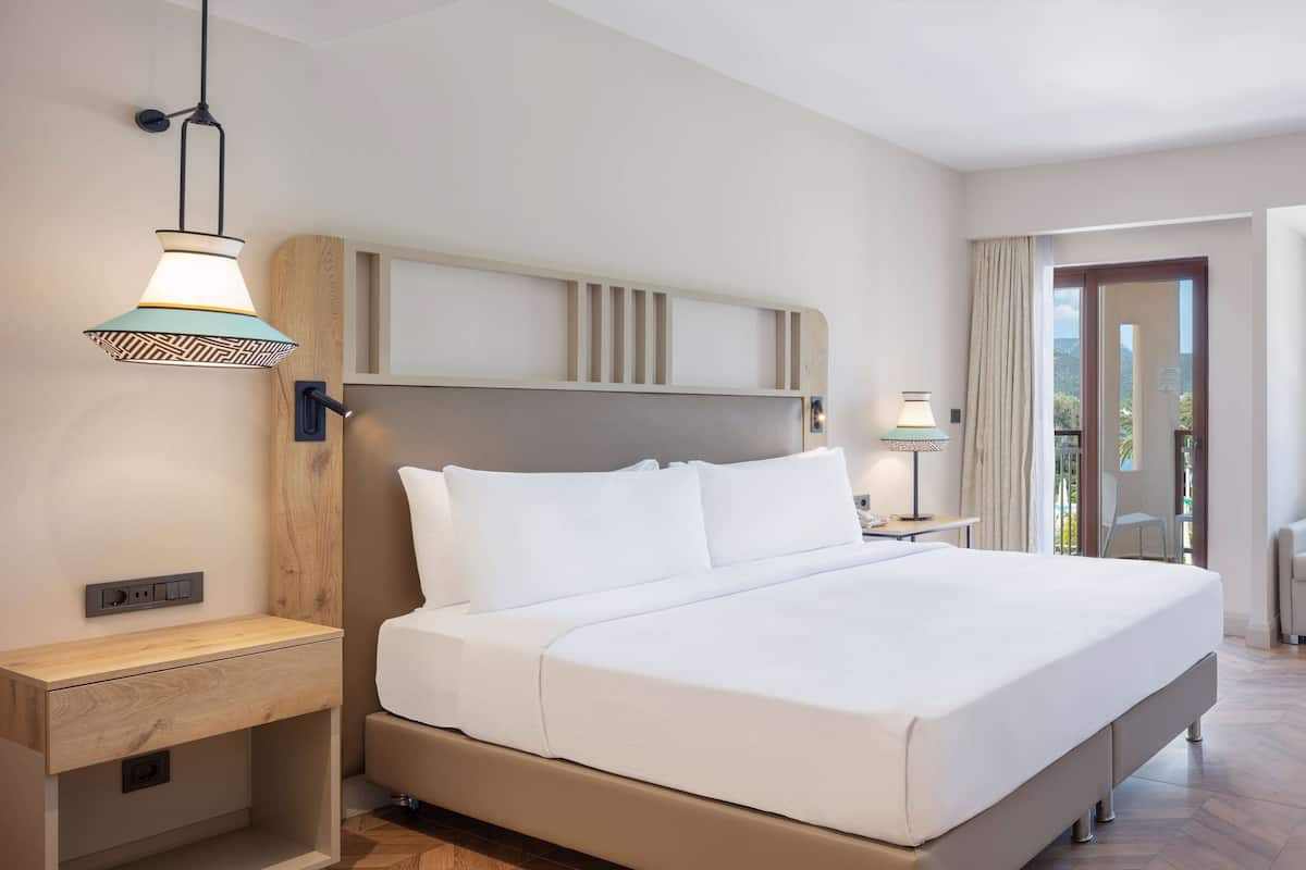 A hotel room with a bed, bedside table, lamp, TV, and a seating area with a sofa and chair.