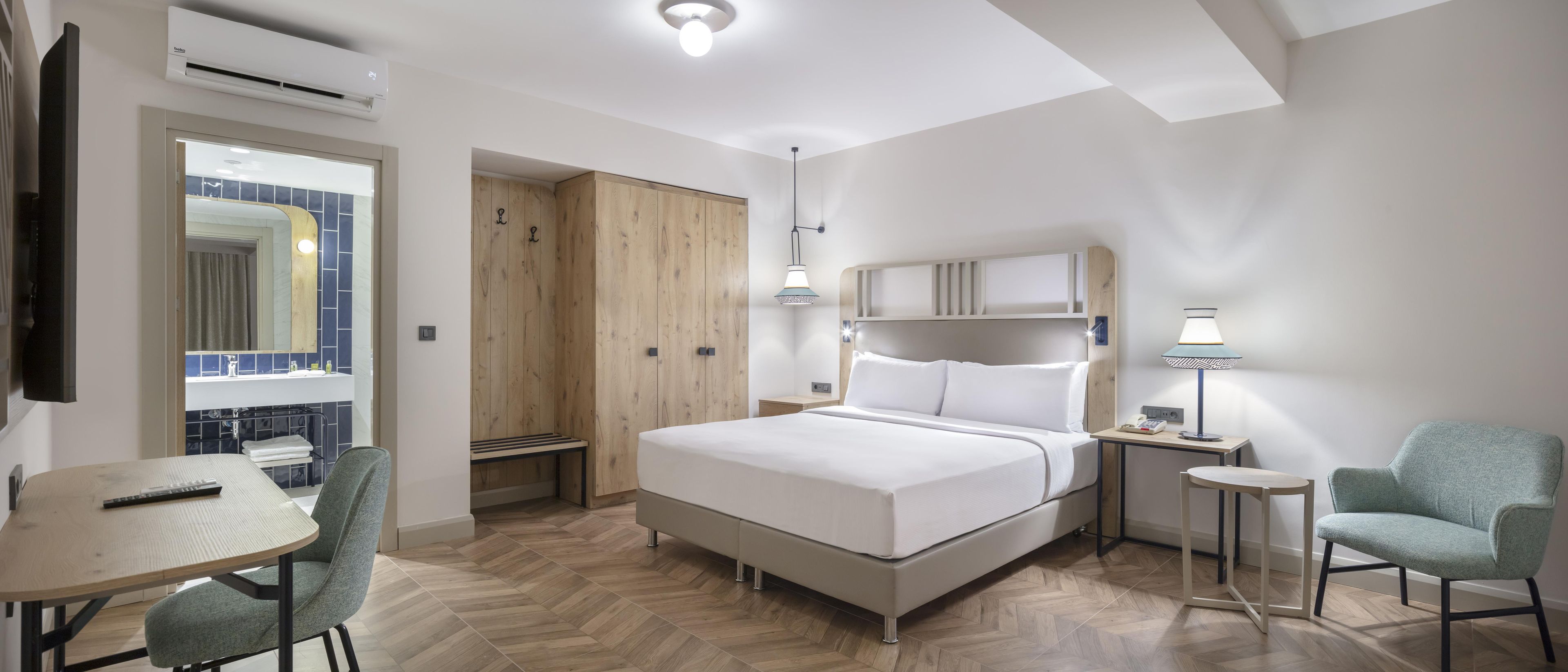 A hotel room with a bed, a desk, a chair, a wardrobe, and a window.