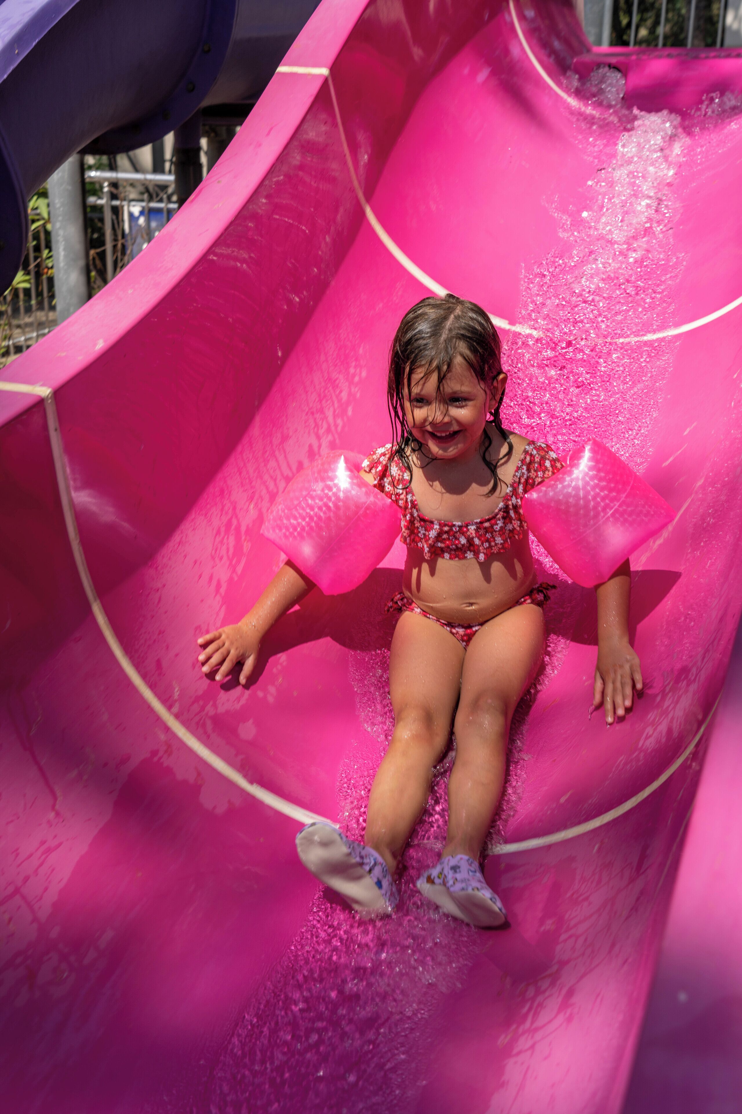 A child sliding down a bright pink water slide.