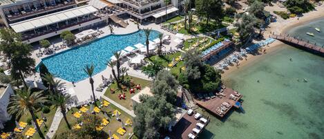 An aerial view of a resort with a large swimming pool, multiple deck areas, and a beach.