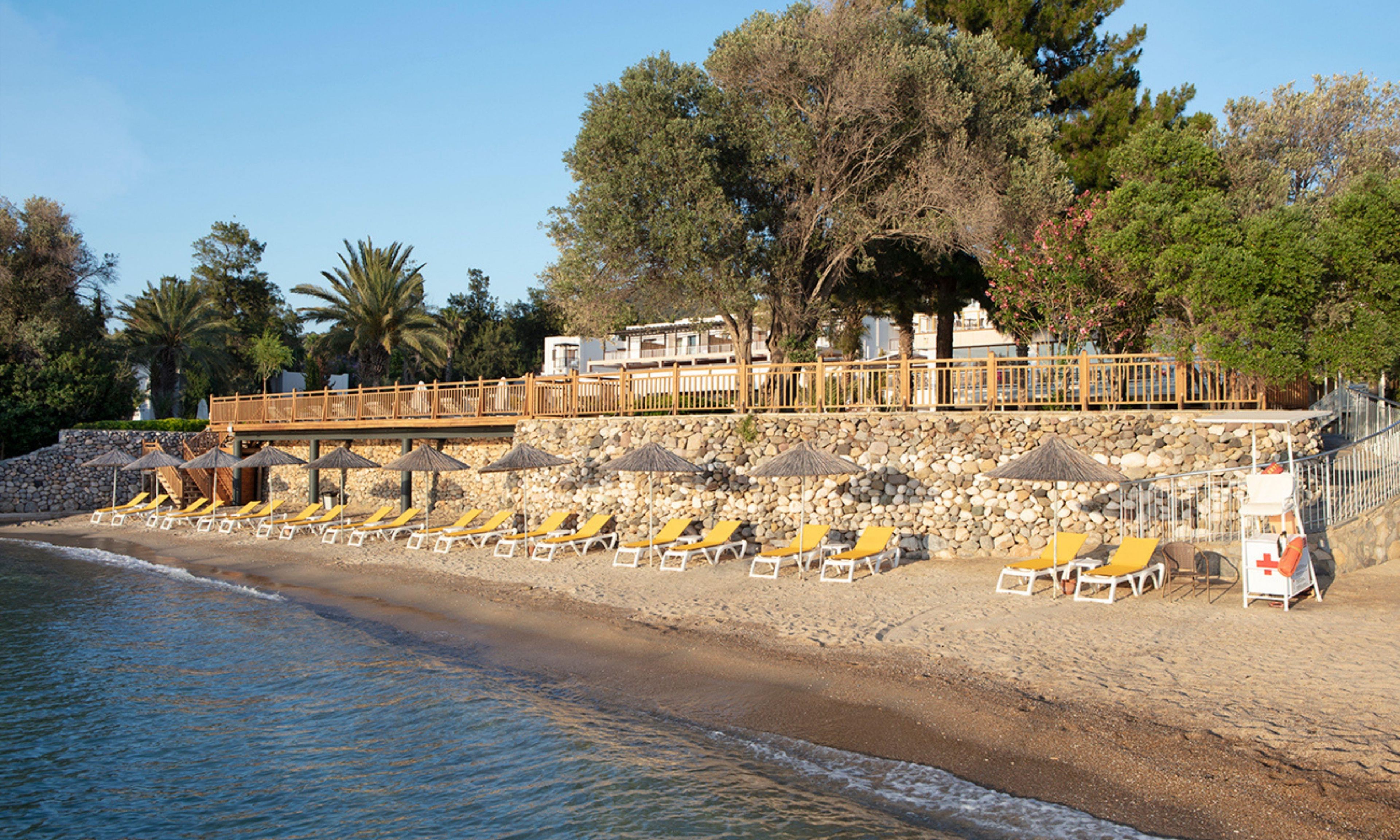 Un hotel sulla spiaggia con muro in pietra, terrazza in legno e lettini prendisole.