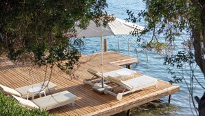 Terraza de madera con sillones de descanso y una mesa, con vistas a un cuerpo de agua.