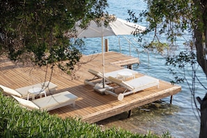 A wooden deck with lounge chairs and a table, overlooking a body of water. - DoubleTree by Hilton Bodrum Işıl Club Ultra All Inclusive Resort (Bodrum)