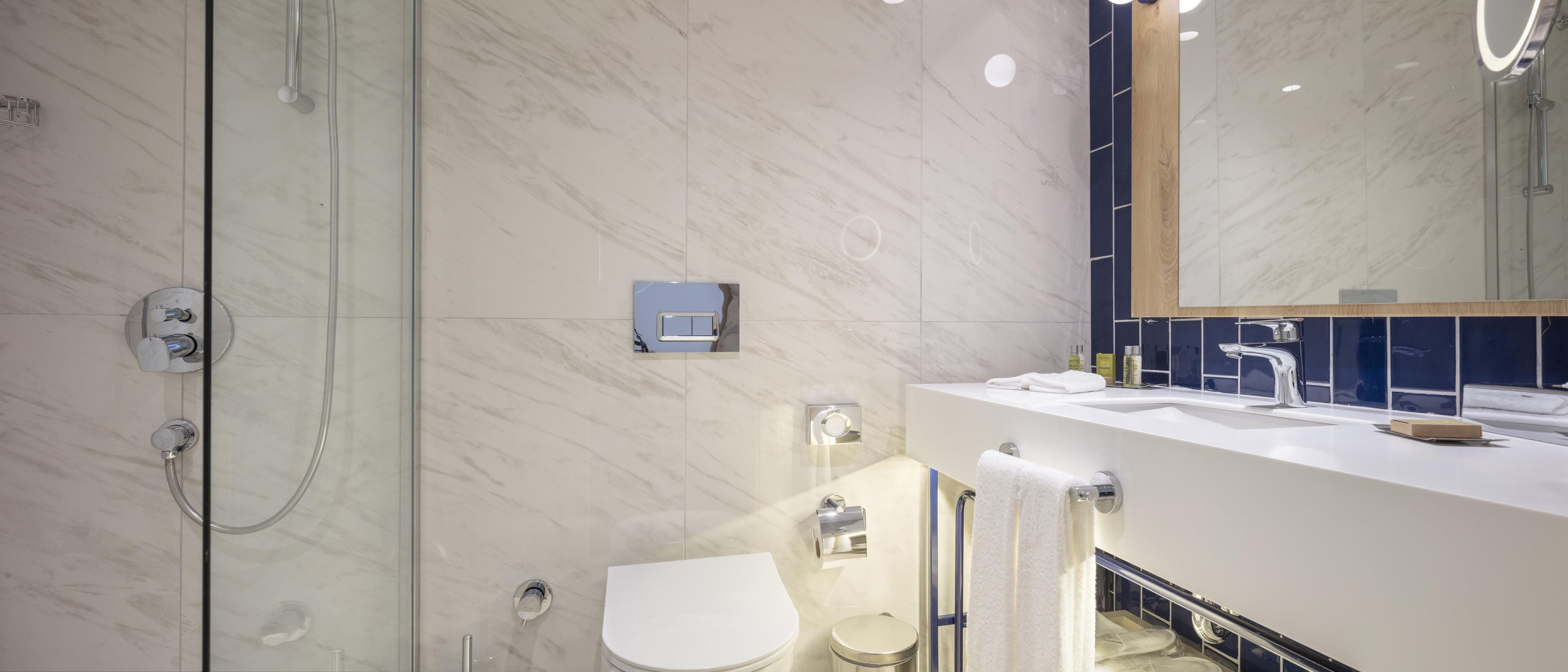 A modern bathroom with a glass shower enclosure, a white toilet, and a sink with a mirror above it.