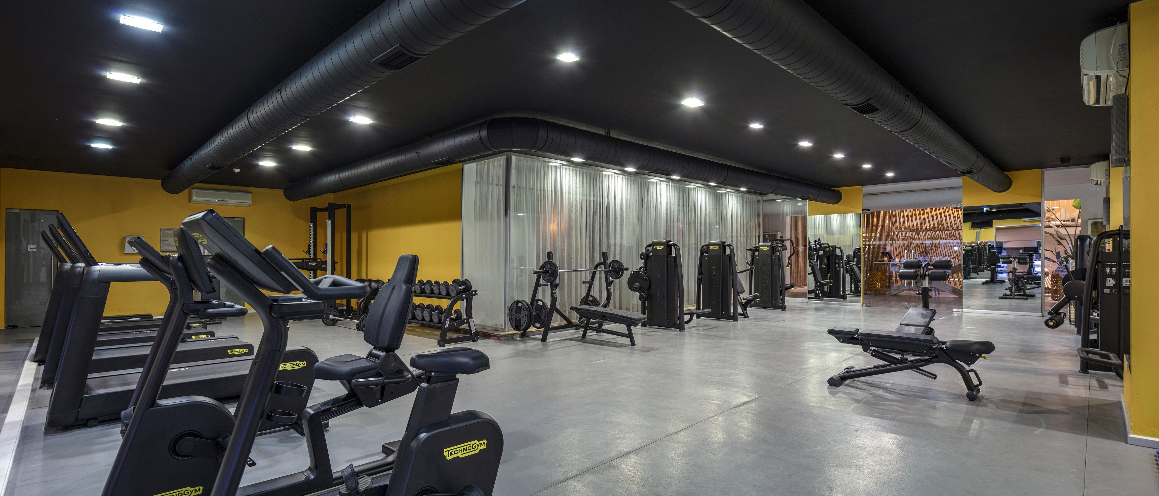A gym with various exercise equipment, including treadmills and weight machines, and a mirrored wall.