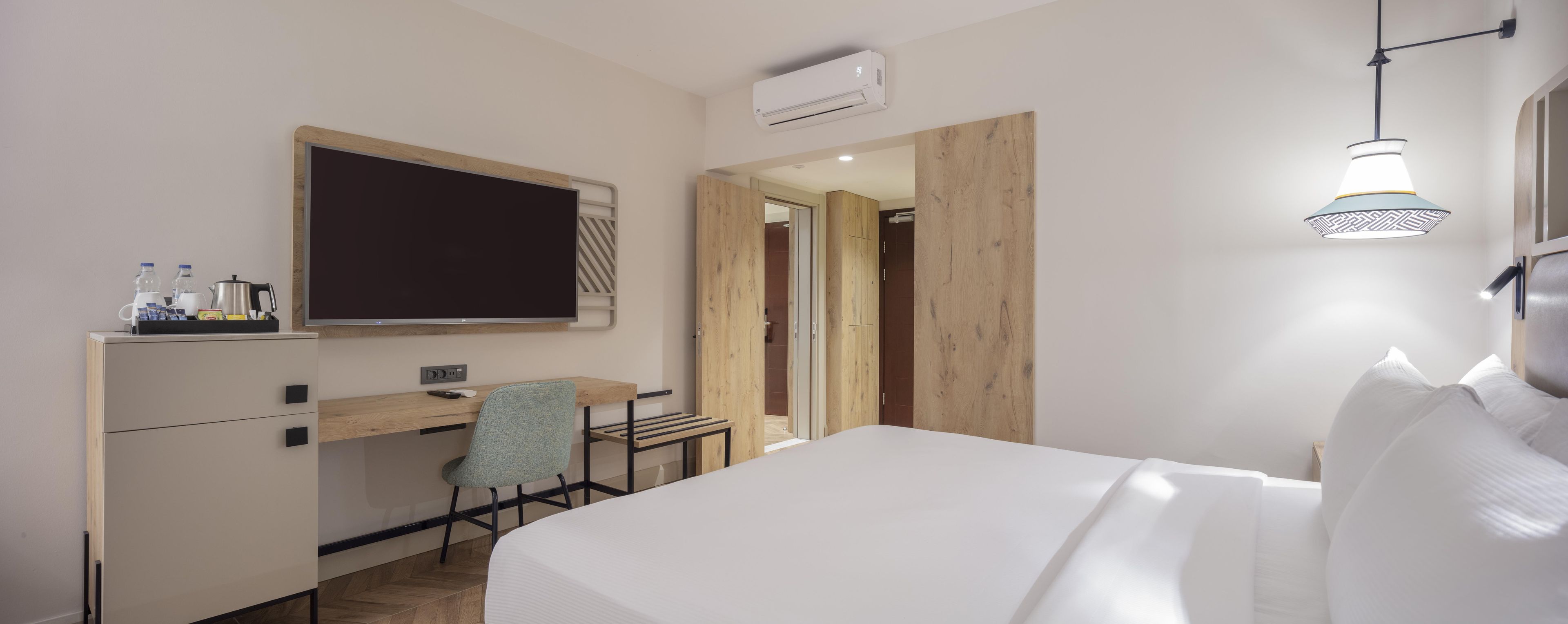 Ein Hotelzimmer mit einem Bett, einem Schreibtisch, einem Stuhl, einem Flachbildfernseher und einer Klimaanlage.