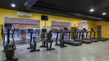 A gym with various exercise equipment, including treadmills and stationary bikes, and a large mirror reflecting the interior.