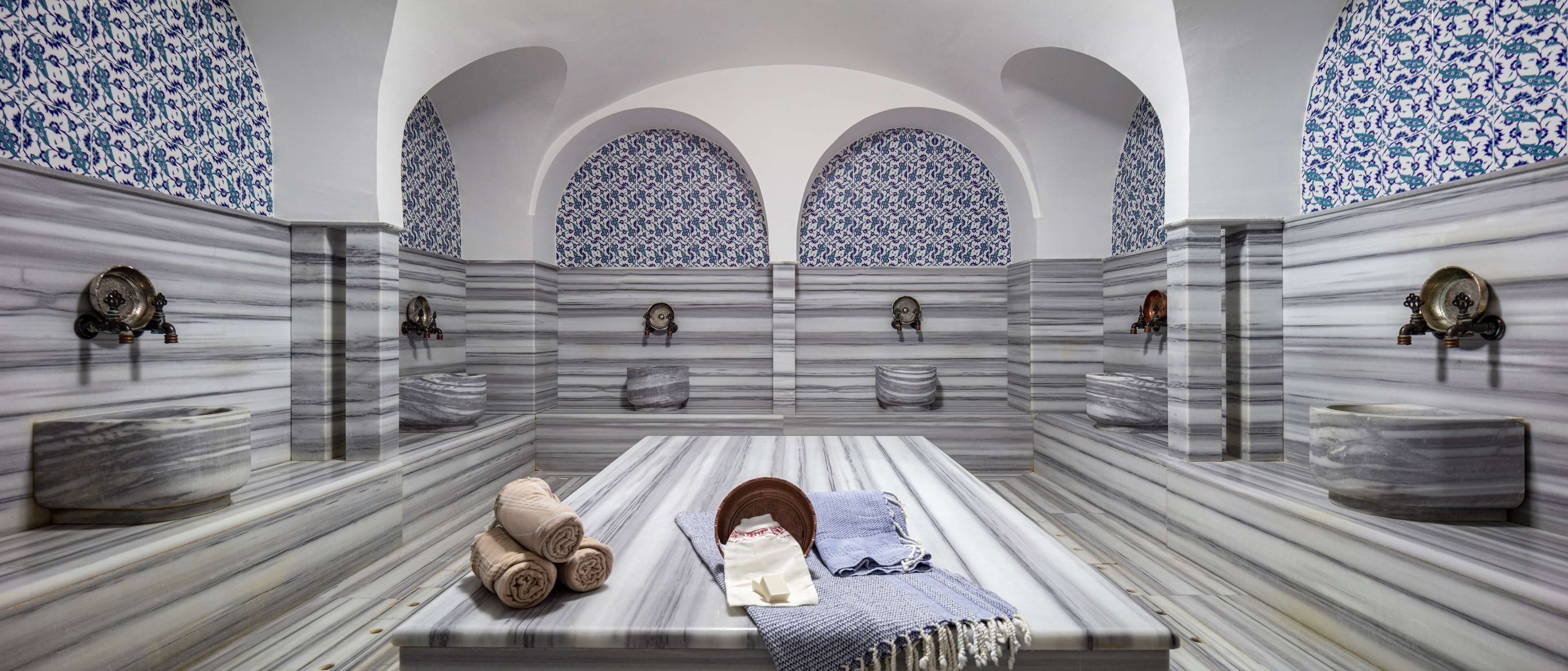 A bathroom with marble walls, a central sink, and three arched niches with decorative plates.