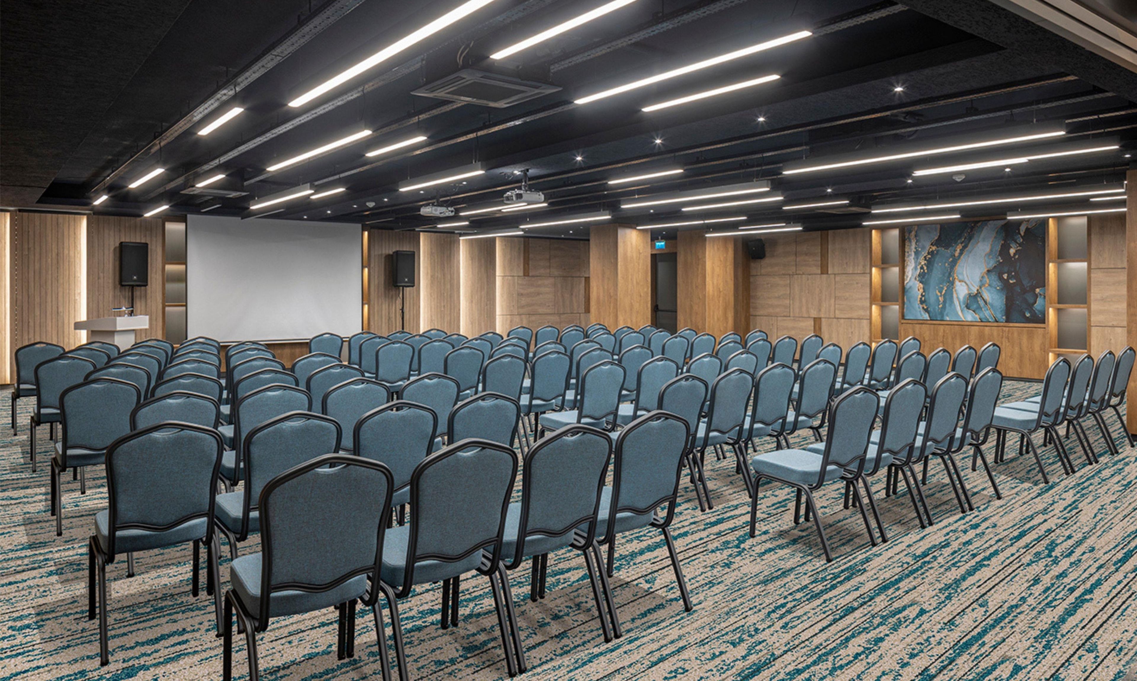 A conference room with rows of chairs, a projector screen, and a large painting on the wall.