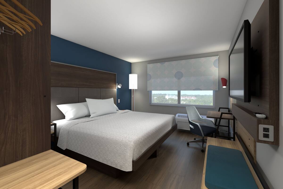 Une chambre d’hôtel moderne dotée d’un grand lit, d’un bureau, d’une chaise, d’une télévision et d’une fenêtre donnant sur la ville.