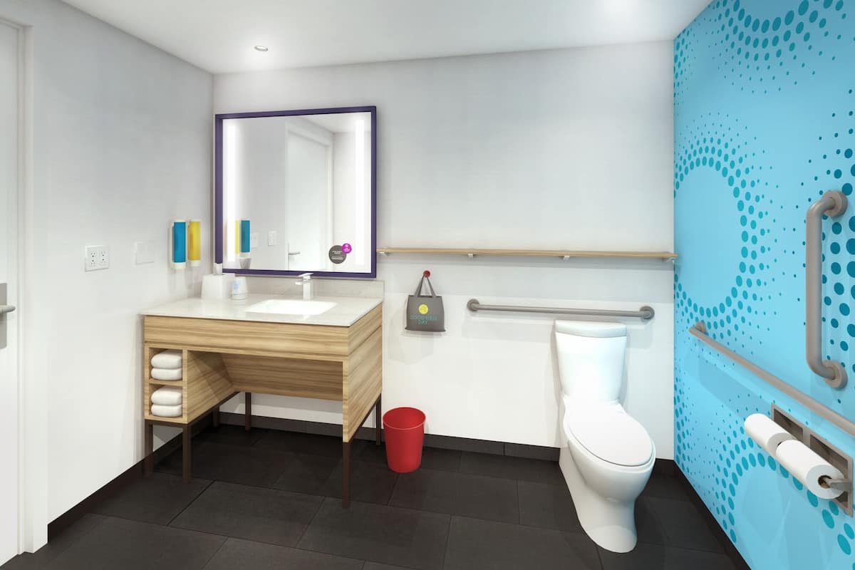 Une salle de bain moderne avec un meuble-lavabo en bois, un lavabo blanc, un miroir, des toilettes et une poubelle rouge.
