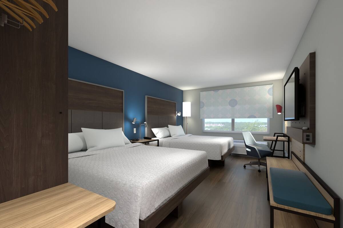 Une chambre d’hôtel avec deux lits, un bureau, une chaise, une télévision et une fenêtre donnant sur un beau paysage.