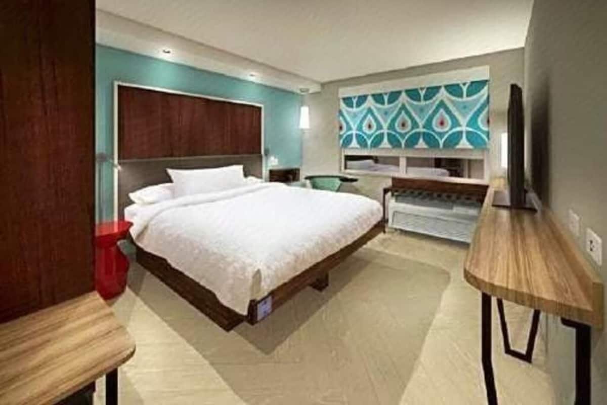 Une chambre d’hôtel avec un lit, un bureau, une chaise, une télévision et un mur décoré d’un motif.