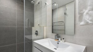 Een moderne badkamer met een groot wit wastafel, een glazen douchecabine en een spiegel boven het aanrecht.