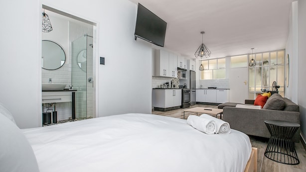 Een moderne hotelkamer met een groot bed, een bank, een klein tafeltje, een televisie en een kitchenette.