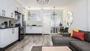 Een moderne keuken met witte kasten, een zwarte kookplaat en een zithoek met een grijze bank en een spiegel.