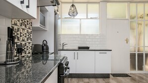 Een moderne keuken met witte kastjes, een zwart aanrecht, een koffieapparaat en een waterkoker.