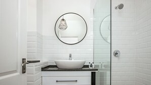 Een moderne badkamer met een wit wastafelmeubel, een ronde spiegel en een douchecabine met glazen wanden.