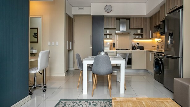 A modern kitchen with a dining area, stainless steel appliances, and a clock on the wall. - Comfortable and Stylish in Rosebank (Johannesburg)