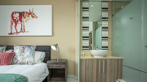 Una camera da letto moderna con un letto, un comodino, una lampada e un grande specchio sopra una toeletta in legno.