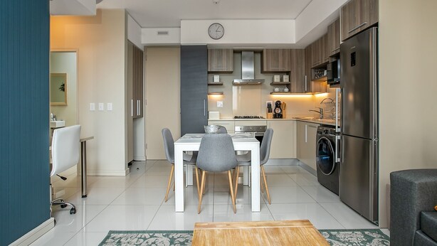 Una cucina moderna con zona pranzo, elettrodomestici in acciaio inossidabile e un orologio appeso al muro.