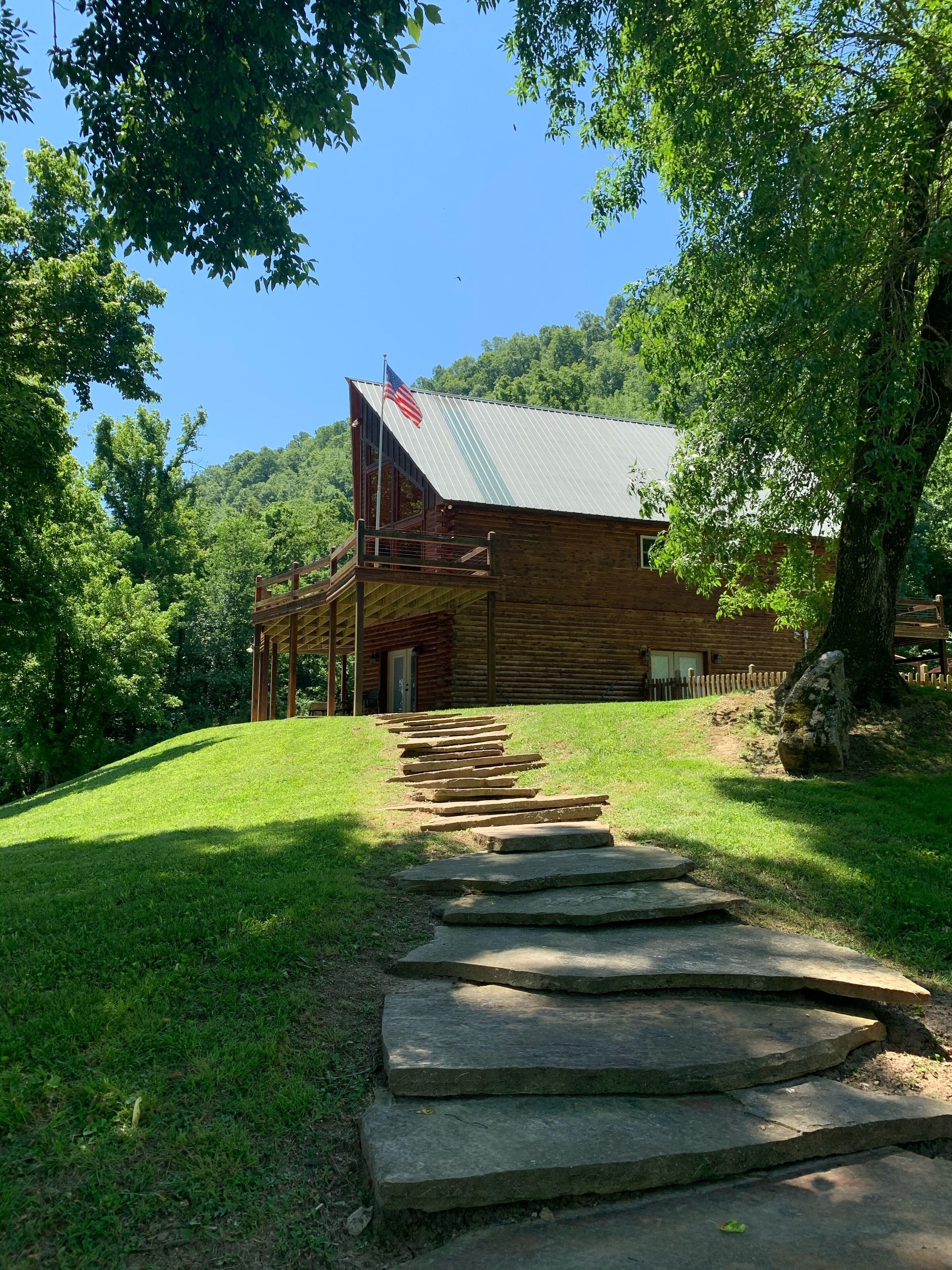 A wooden cabin with a metal roof, a flag, and a stone staircase leading to the entrance.