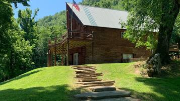 A wooden cabin with a metal roof, a flag, and a stone staircase leading to the entrance.