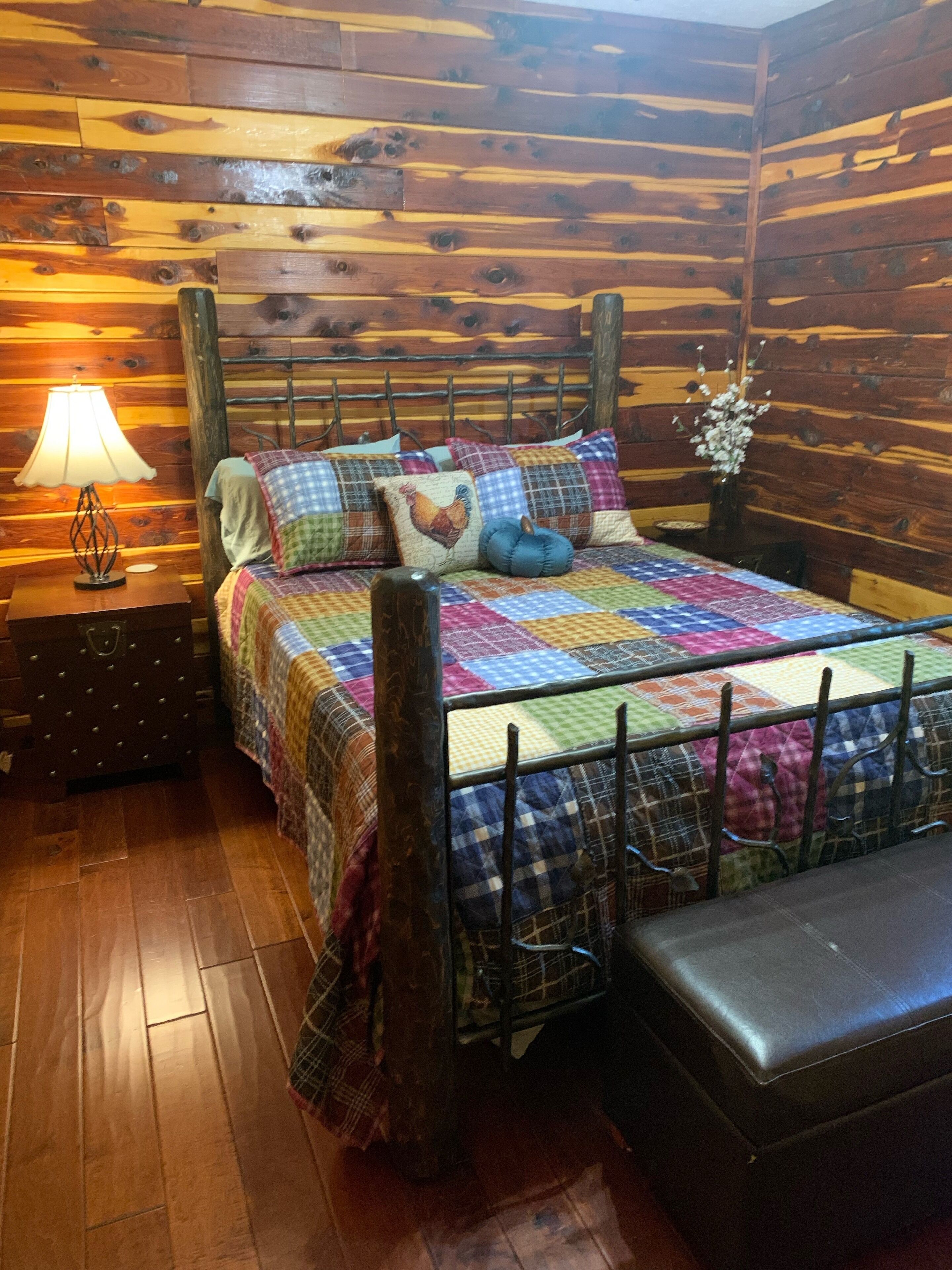 A wooden cabin-style room with a bed, a nightstand, a lamp, and a bench.