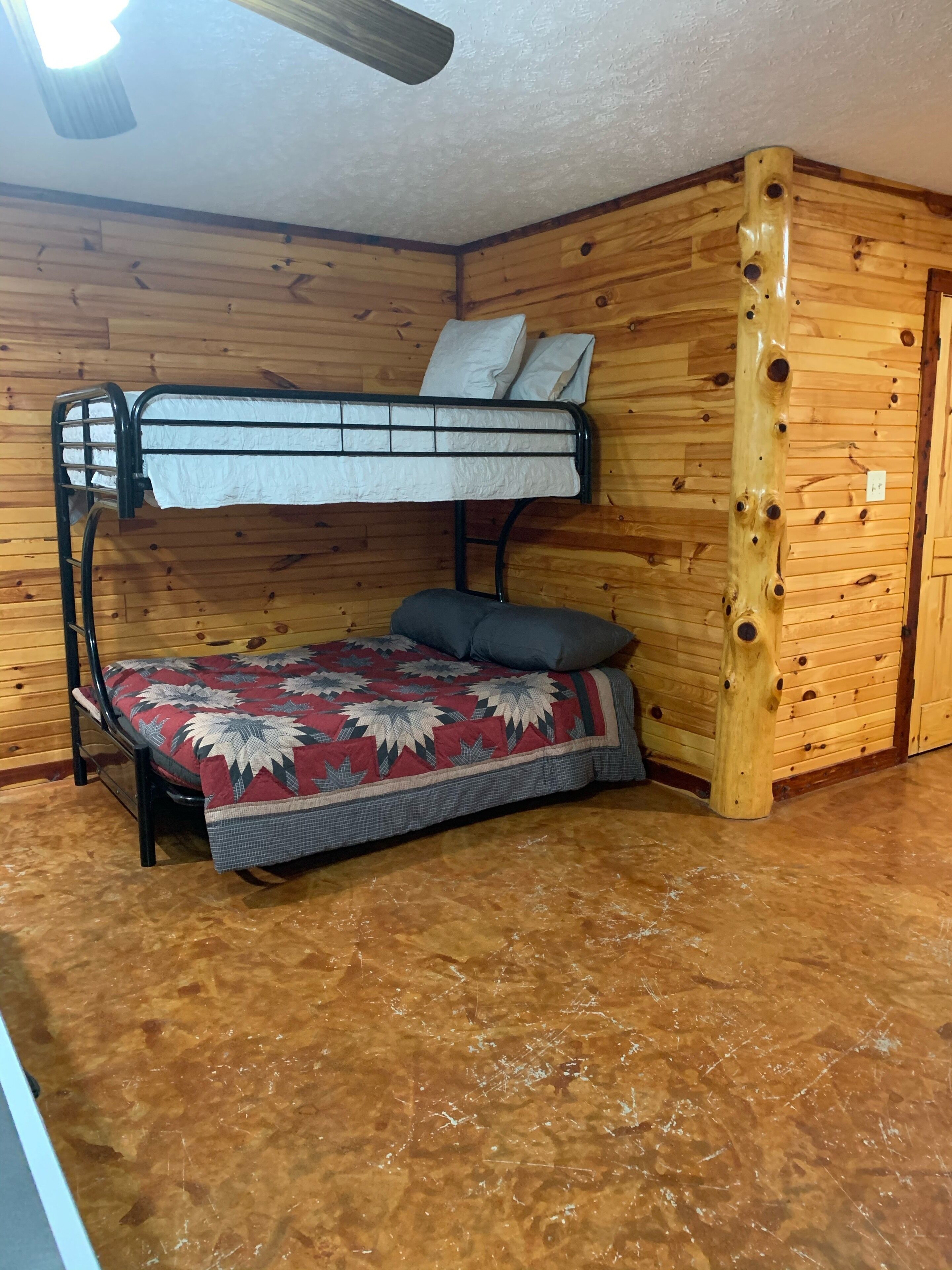 A bunk bed with a patterned bedspread and pillows, wooden walls, and a ceiling fan.