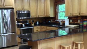 A modern kitchen with wooden cabinets, stainless steel appliances, a granite countertop, and a bar stool area. - SECLUDED WHITE RIVERFRONT CABIN -SLEEPS 2-10, GREAT FAMILY & FISHERMEN GETAWAY (Norfork)