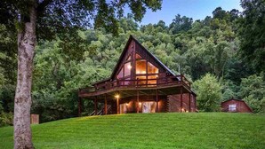 A wooden cabin with a large porch, surrounded by lush greenery. - SECLUDED WHITE RIVERFRONT CABIN -SLEEPS 2-10, GREAT FAMILY & FISHERMEN GETAWAY (Norfork)