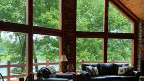 A spacious room with a wooden ceiling, large windows, a ceiling fan, a fireplace, leather sofas, and a dining table with chairs. - SECLUDED WHITE RIVERFRONT CABIN -SLEEPS 2-10, GREAT FAMILY & FISHERMEN GETAWAY (Norfork)