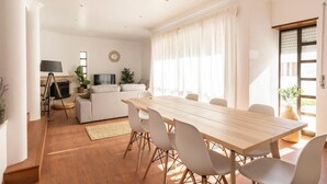 A spacious living area with a wooden dining table, white chairs, a sofa, and a fireplace. - Ericeira Paradise House & Suites (Mafra)